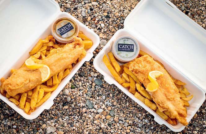 Two boxes of fish and chips from Catch sitting on the sand