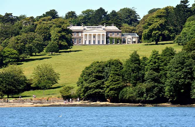 Green lawns leading up to a stately house with a river at the bottom at Trelissick in Cornwall
