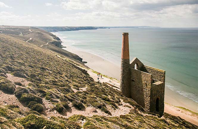 The old engine house sits on the cliff while people walk along the coast path