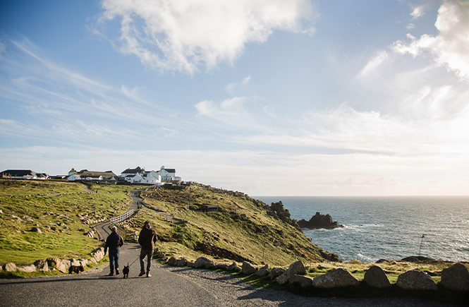 Two people walking a dog along the coast path at Land's End in West Cornwall