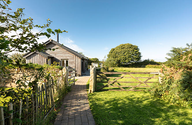 A pathway leads to a barn conversion amid trees and fields.