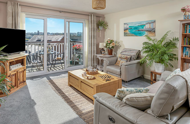 Large windows and a balcony open up from the living room with sofas, desks and boardgames