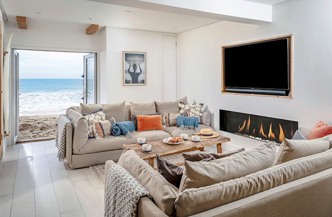 A sitting area with two sofas and a fire has glass doors leading directly to the sand.