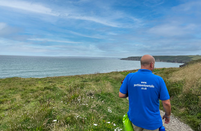 A man in a blue t-shirt walks along the coast path