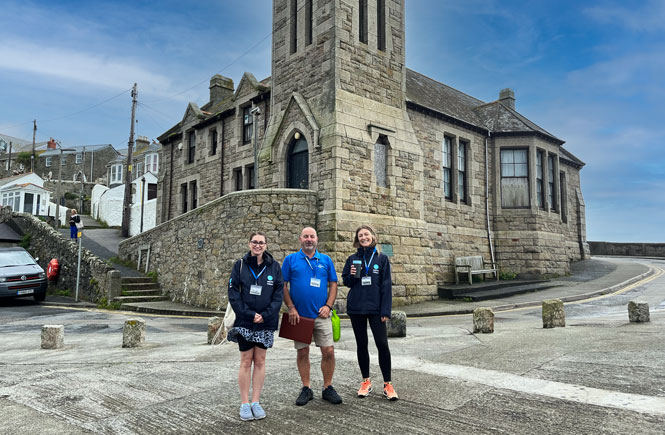 three people stand in front of the iconic Porthleven clock tower