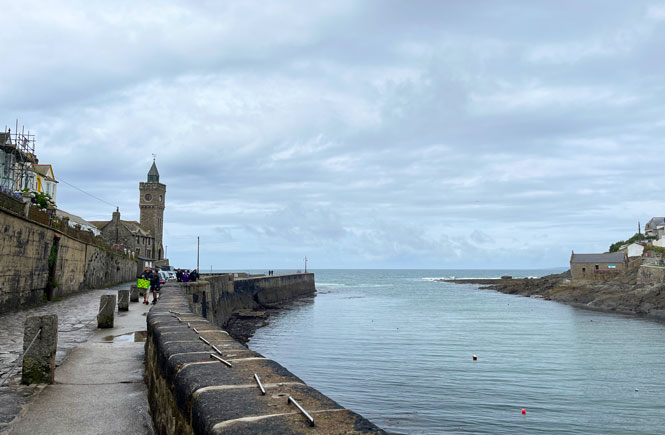 Porthleven harbour on a grey day, with some people walking along the harbour.