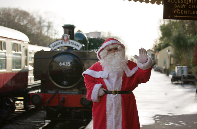 Father Christmas waving in front of a steam train at Bodmin and Wenford Railway in Cornwall
