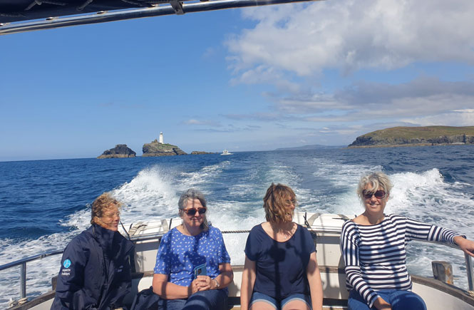 Godrevy Lighthouse in the distance behind the Aspects Holidays team enjoying the boat trip with Black Pearl