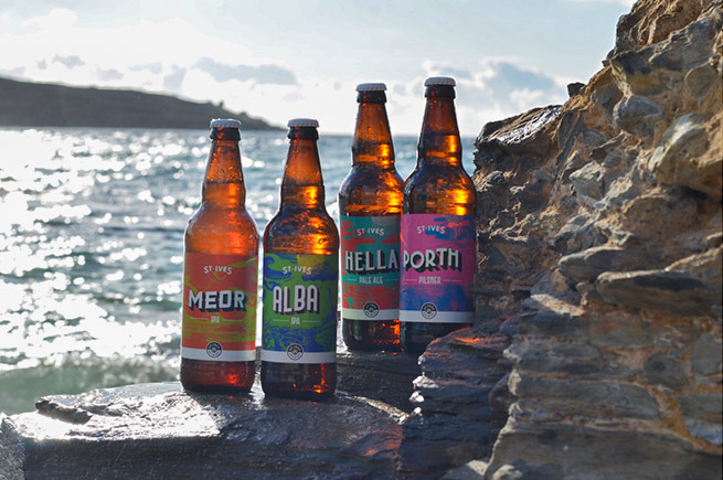 A selection of St Ives Brewery beers sitting on some rocks in front of the ocean