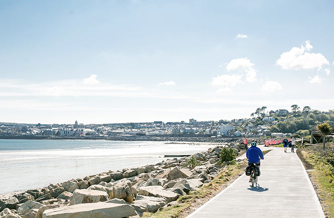 A cyclist rides along the path by the sea