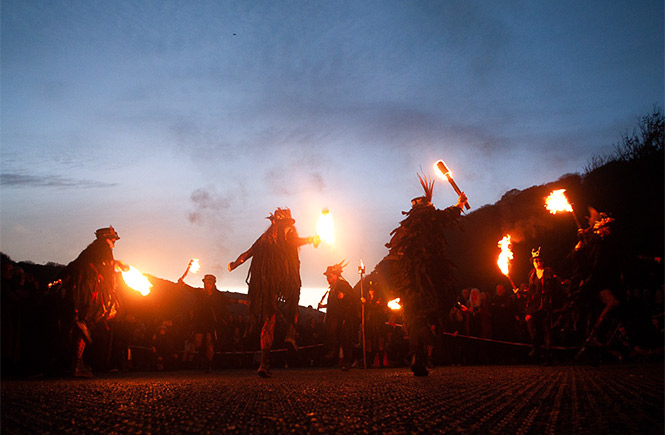 People dancing round with torches of fire at dusk at The Dark Gathering in Cornwall