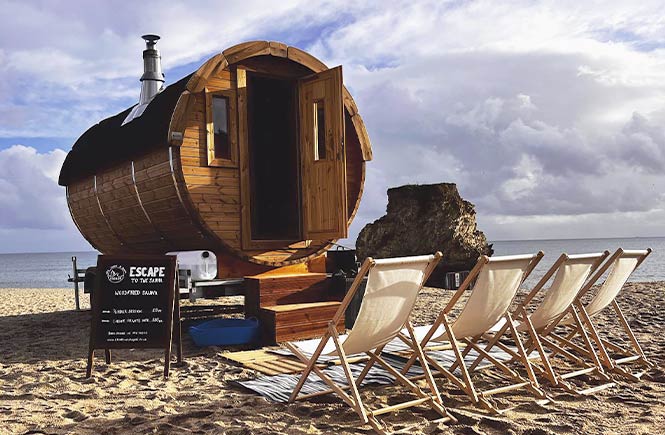 A wooden, barrel-shaped sauna on the beach with Escape Swims
