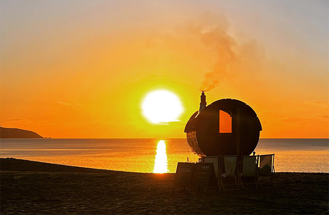A wood-fired sauna on the beach at sunset in Cornwall