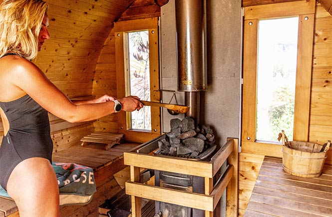 Someone adding water and essential oils to the hot coals in the wood-fired sauna in Cornwall