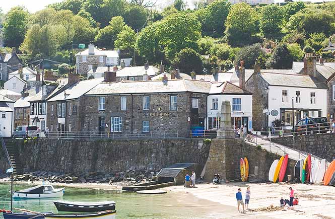 A small patch of sandy beach in the harbour of Mousehole with The Ship Inn on the harbour front above
