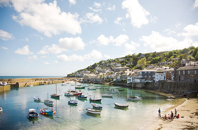 The beautiful Mousehole harbour with boats in the water and cottages above the beach